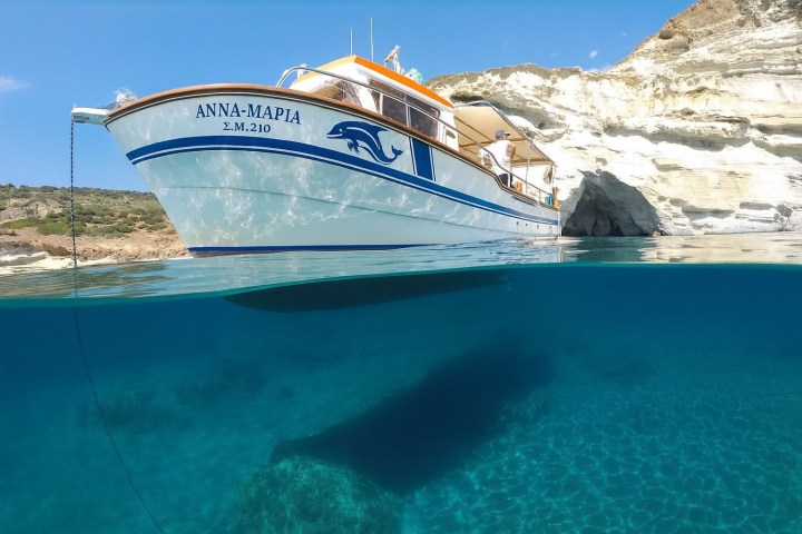 Boat with dolphin design floats in clear water near rocky cliffs under a blue sky.