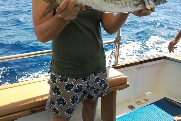Person holding a fish on a boat with the ocean in the background.