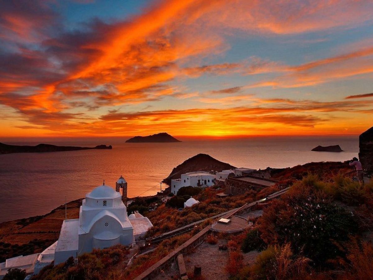 Sunset over Greek island with white buildings and sea view.