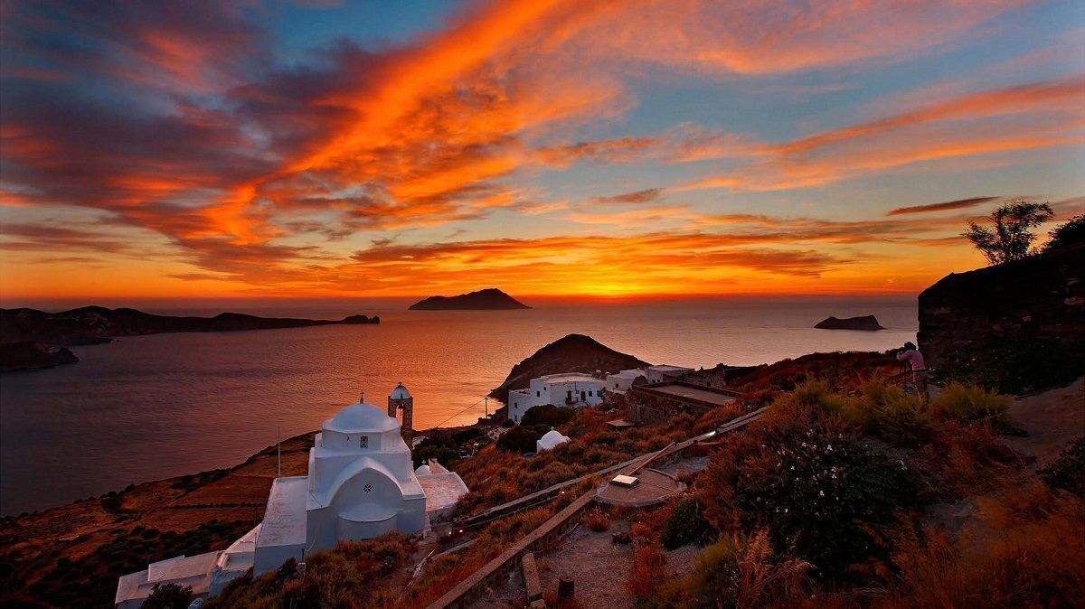 Sunset over Greek island with white buildings and sea view.